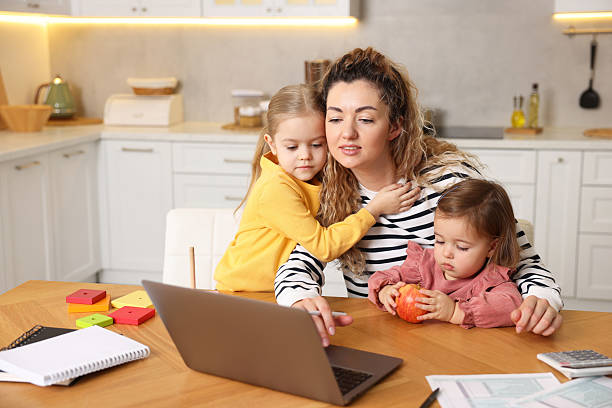 istock Single mother working on laptop and her daughters at table in kitchen 2210968866