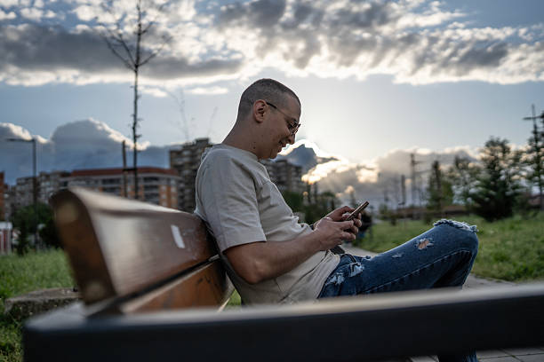 istock Man Using Smartphone on Bench in City Park During Sunset 2210969035