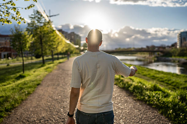 istock Man Walking on a Pathway in a Beautiful Riverside Park at Sunset 2210969047