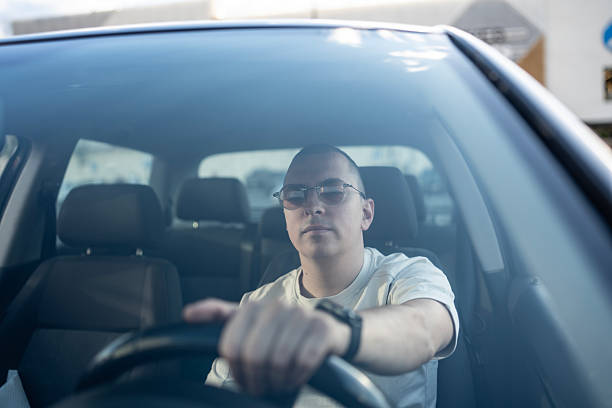 istock Man Driving a Car Seen Through Front Windshield in Urban Setting 2210969132