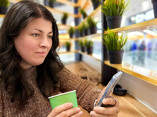 istock Woman using smartphone and drinking coffee in a shopping mall cafeteria 2210969638