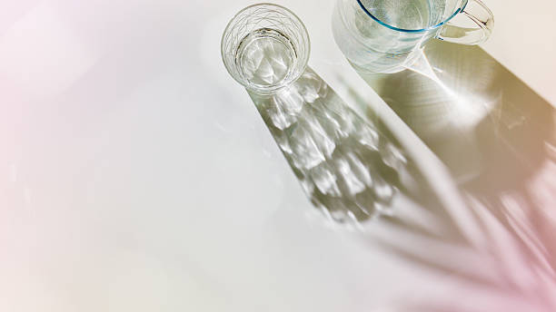 istock Water Glasses and water jug with palm leaf Shadows and sunlight Reflection on white, banner, colored minimal aesthetic top view summer still life, refraction throug crystal cups, caustics 2210969720