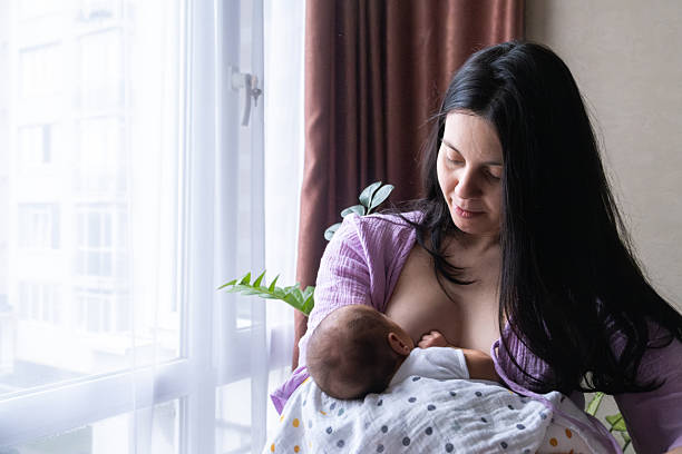 istock Mother Breastfeeding Baby by Window 2210975196