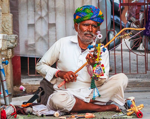 Udaipur, India - 07 August, 2018:A captivating image of an Indian musician playing a traditional instrument in the open air, set against the scenic backdrop of Udaipur, Rajasthan. The musician’s focused performance showcases the rich cultural heritage of Rajasthan, with the instrument adding a melodic charm to the vibrant atmosphere.