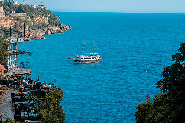 Antalya, Turkey – 08, May, 2023: Tourist Boat in the Blue Sea. People sitting in a cafe.