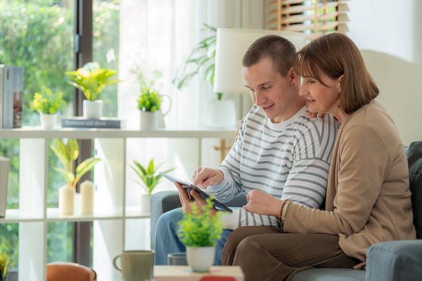 istock Affectionate moment of a son guiding his retired mother through using a digital device for email, video calls, and online services. Technology for senior adults, learning together, lifestyle support, and emotional wellbeing indoors on the sofa. 2210983772