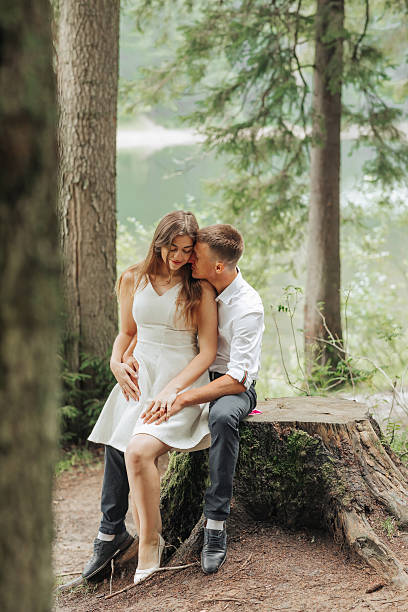 Young couple, seen through a car window, standing close together in the forest, kissing and holding each other. Surrounded by trees and soft natural light, it’s a quiet and intimate moment, full of love and peace in nature.