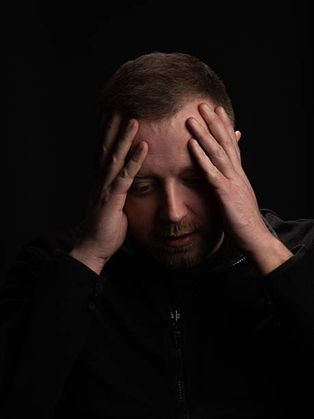 istock Man Expressing Stress with Hands on Head Against Dark Background 2210993253