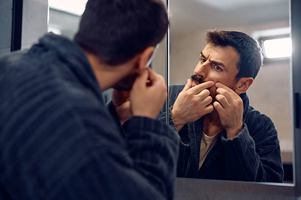 istock Reflection in a mirror of a man squeezing a pimple. 2210995953