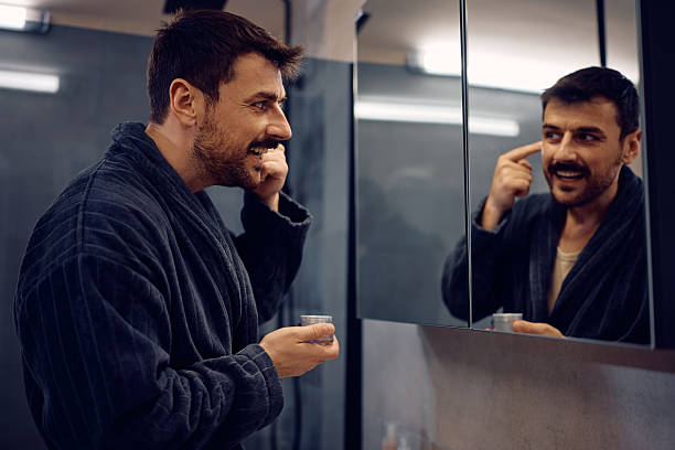 istock Happy man using moisturizer while taking care of his face skin in the bathroom. 2210995969