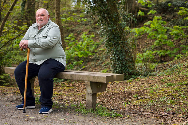 istock Overweight man with a walking stick resting on a bench 2210999888