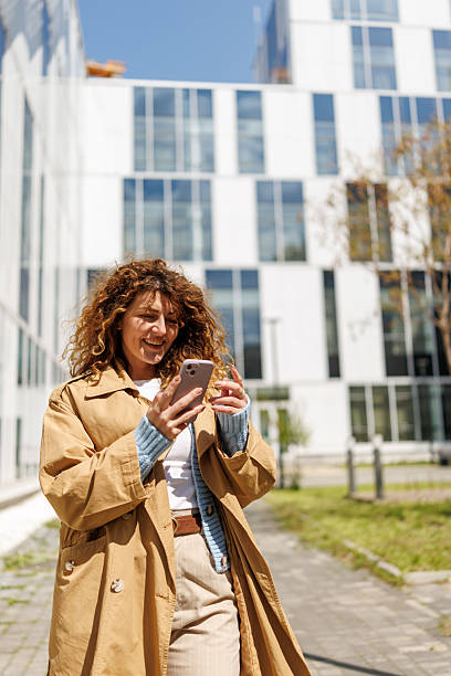 istock Smiling woman using smartphone outdoors near modern office building 2211000173