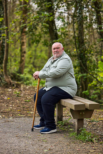 istock Overweight man with a walking stick resting on a bench 2211000420