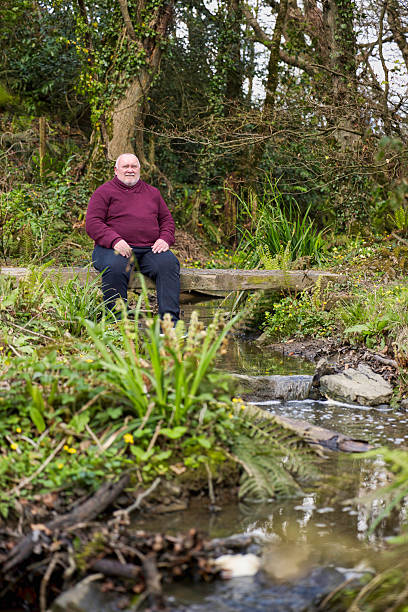 istock Overweight man resting on a bridge spanning a brook 2211000522