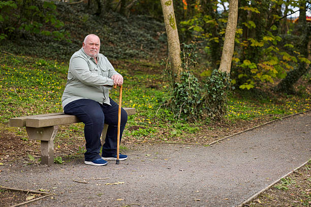 istock Overweight man with a walking stick resting on a bench 2211001317