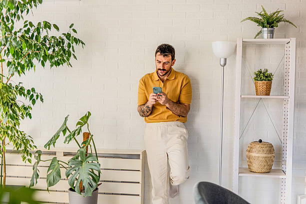 istock Young man using smartphone in modern apartment with many plants 2211001351