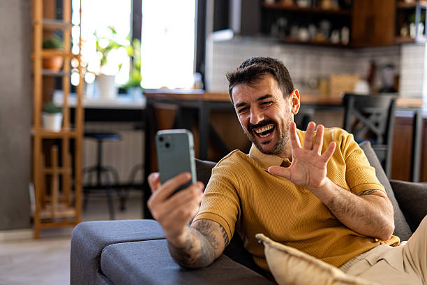 istock Happy man waving during video call on smartphone at home 2211001383