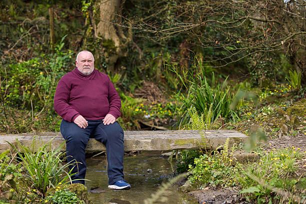 istock Overweight man resting on a bridge spanning a brook 2211001766