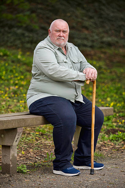 istock Overweight man with a walking stick resting on a bench 2211001950