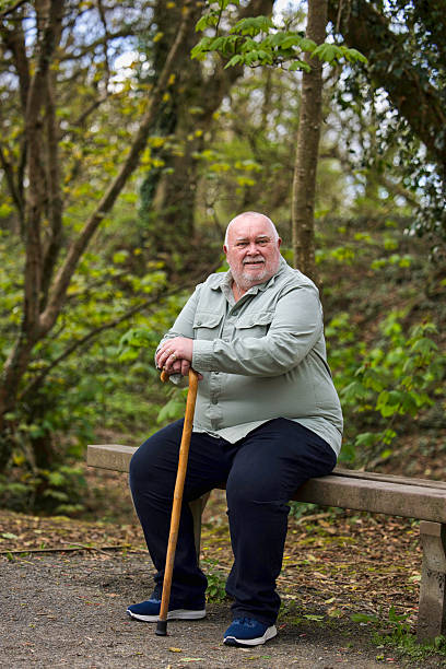 istock Overweight man with a walking stick resting on a bench 2211002711