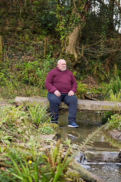 istock Overweight man resting on a bridge spanning a brook 2211003079