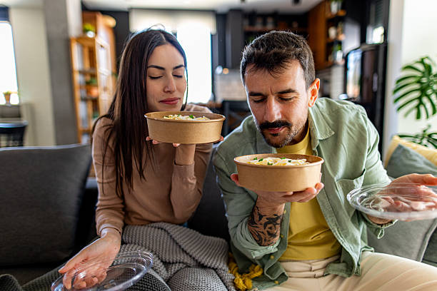 Young couple enjoying the aroma of their takeaway pasta, sitting comfortably on their sofa at home