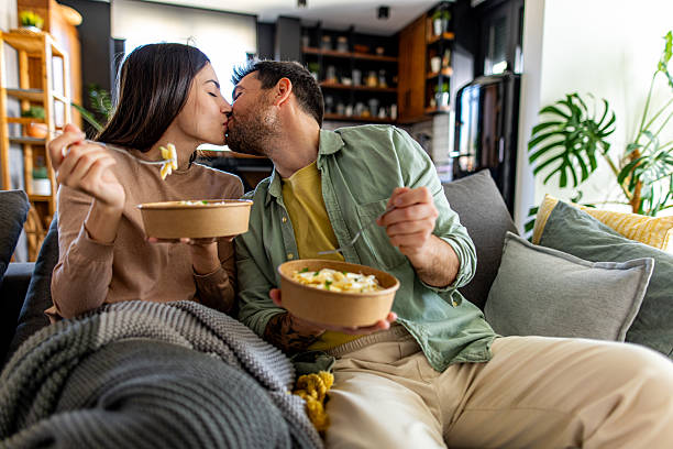 istock Young couple kissing while eating pasta on the sofa at home 2211004160