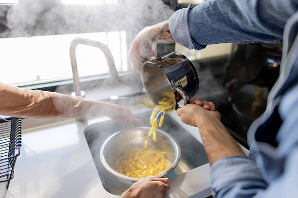 Couple draining pasta in kitchen sink