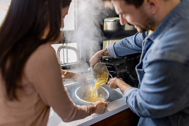 istock Couple draining pasta in kitchen sink 2211005763