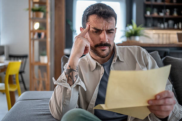 istock Worried man reading a letter on the sofa at home 2211006965