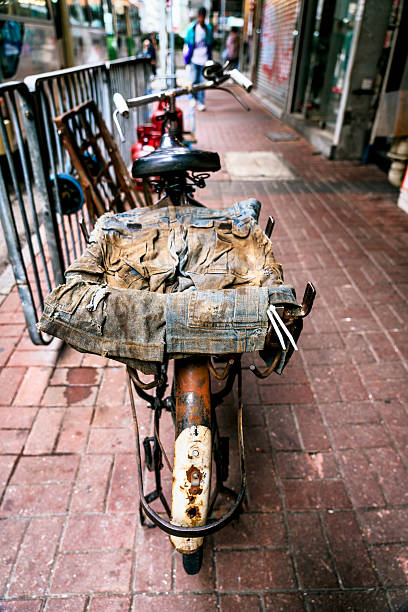 Rusty vintage bicycle parked on a sidewalk in hong kong, featuring worn clothes draped over the rear rack