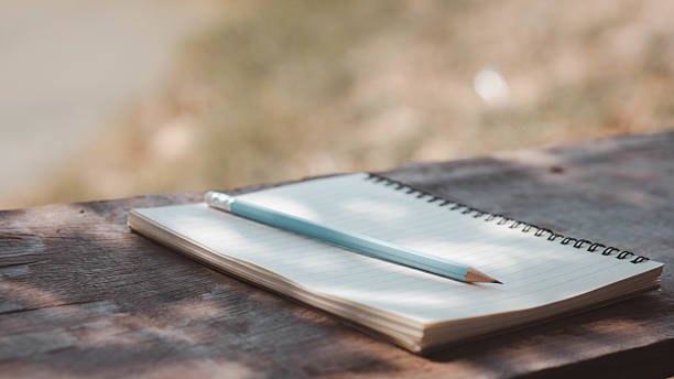 istock A blank spiral notebook and a pencil are placed on a rustic wooden table. An open notebook with a pencil placed on top, resting on a wooden table inside the house. 2211012792