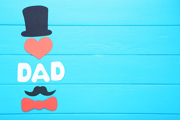 Text Dad with paper hat, mustache and bow tie on blue wooden table