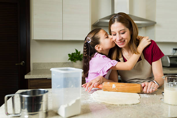 istock Daughter kissing mother while making dough in kitchen 2211024098