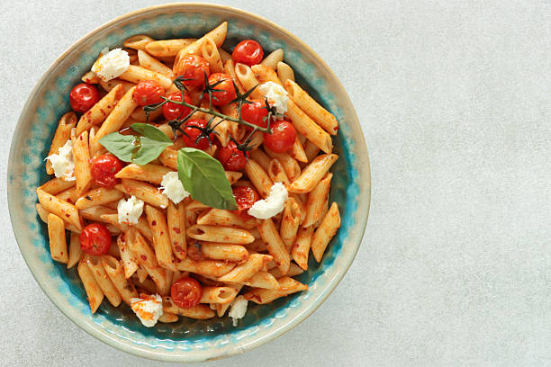 Image of overhead view of penna pasta dish, burrata cheese, cherry tomatoes, basil leaves, buffalo mozzarella balls / tasty italian cuisine styled copyspace stock photo