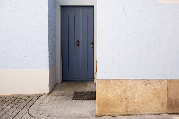 A stylish blue door set in a light blue stucco wall, featuring classic metal hardware and a stone-tiled base.