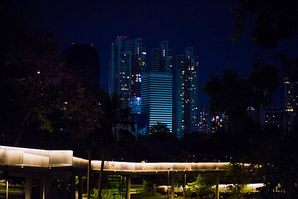 Bangkok night skyline behind Benjakitti Park in Khlong Toie. In foreground is illuminated elevated skywalk through park
