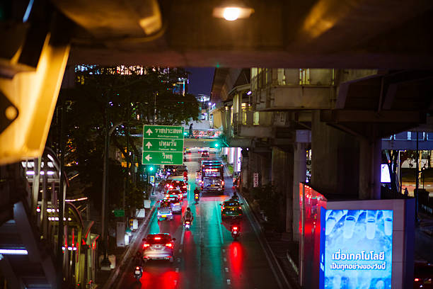 High angle view of Phloen  Chit Road in Bangkok downtown at night. View from pedestrian footbridge over street below BTS skytrain. Traffic is ruling towards west. Below BTS are digital banners and screens for advertising at columns.