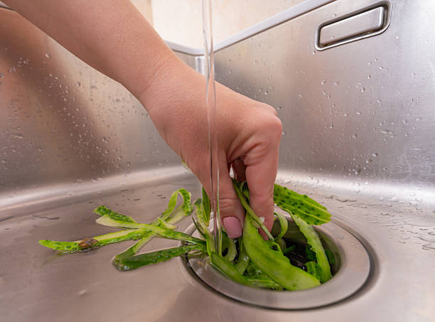 istock Hand pushing vegetable scraps into a kitchen sink drain with running water 2211032192