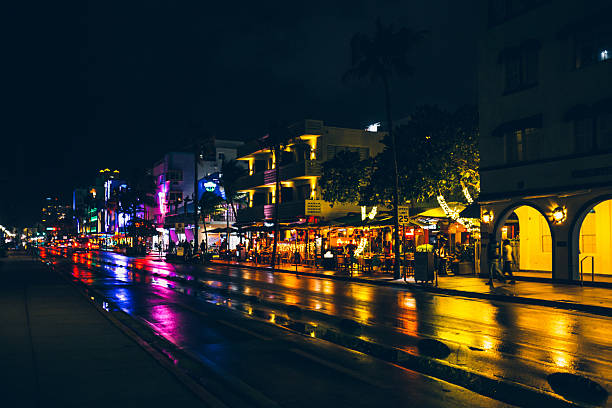 Night scene on Collins Avenue in Miami Beach with car headlight trails and glowing streetlights.