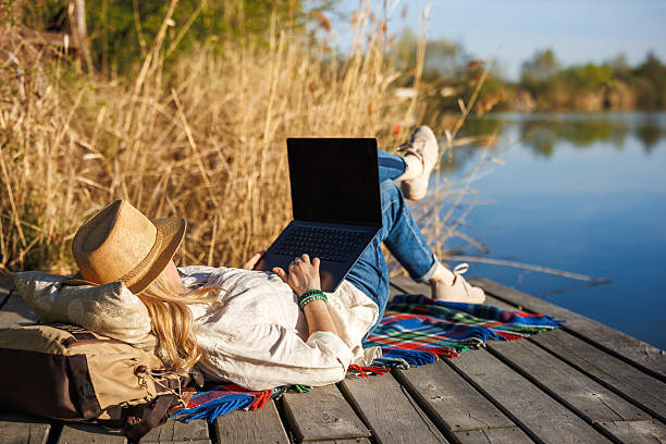 istock Female freelancer reclining by the lake with laptop enjoying nature while remote working 2211038251