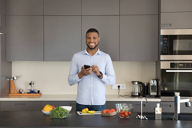 istock Man standing in kitchen with smartphone smile looks at camera 2211064889