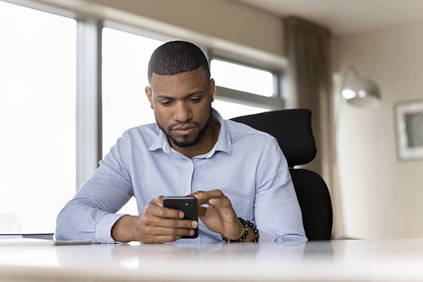 istock Successful serious millennial African businessman using smartphone seated at workplace 2211065233