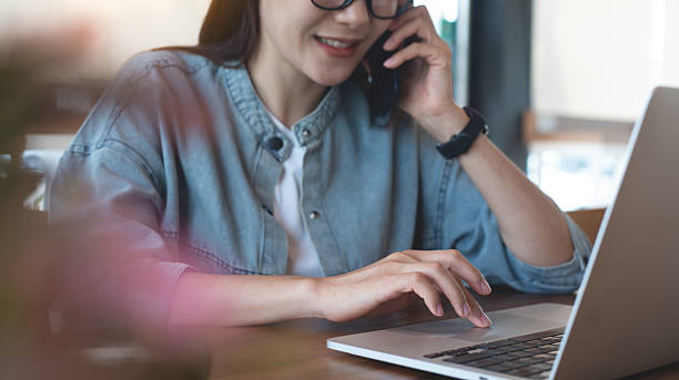 istock Siling young asian business woman talking on mobile phone during working on laptop computer at coffee shop. Happy freelancer having a phone call via smartphone, online working from home office 2211073128