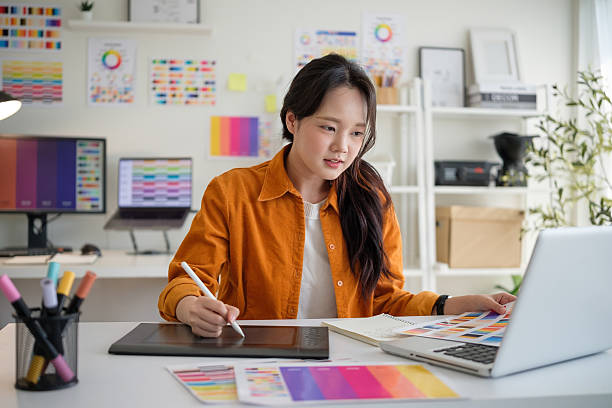 istock Young female graphic designer using a digital drawing tablet in a creative workspace filled with colour charts. 2211077734