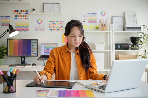 istock Young female graphic designer using a digital drawing tablet in a creative workspace filled with colour charts. 2211077736