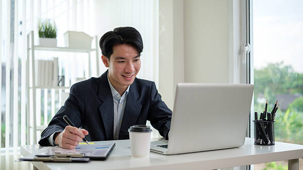 istock Confident male office worker smiling while reading online reports, holding a pen and working on paperwork. 2211077844