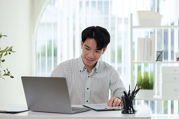 istock Asian businessman focused on reviewing documents and data on a clipboard while working on a laptop.Asian businessman focused on reviewing documents and data on a clipboard while working on a laptop. 2211077866