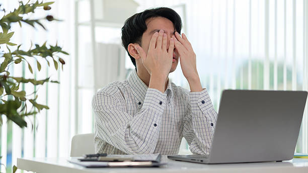 istock Frustrated Asian businessman covering his face with hands while working on a laptop in a bright modern office. Concept of workplace stress, burnout, or deadline pressure. 2211077867