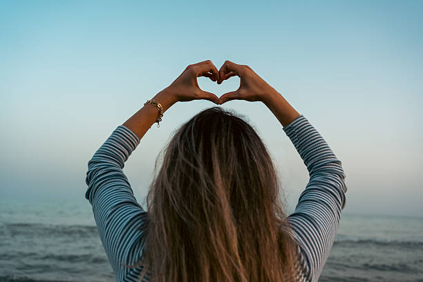 A woman makes a heart sign with her hands on the beach. High quality photo